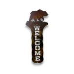 Hand-painted vertical metal welcome sign with grizzly bear, rustic weathered finish, and mountain cabin wilderness decor style.
